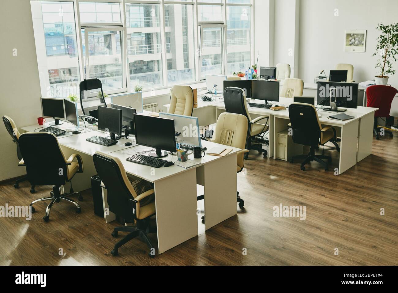 Niemand in modernen Büro mit großen Fenster und Schreibtisch mit Computern und Tassen, covid-19 Konzept Stockfoto