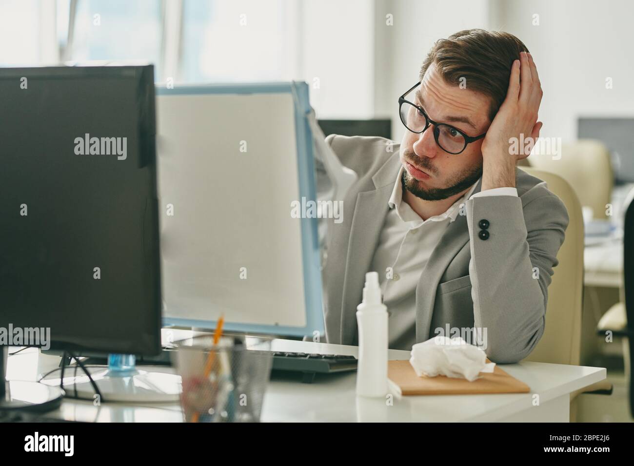 Gereizt jungen Geschäftsmann in Brillen sitzen am Schreibtisch und Blick auf den Computer-Bildschirm, während mit Arbeitsproblemen wegen Coronavirus Quarantäne Stockfoto