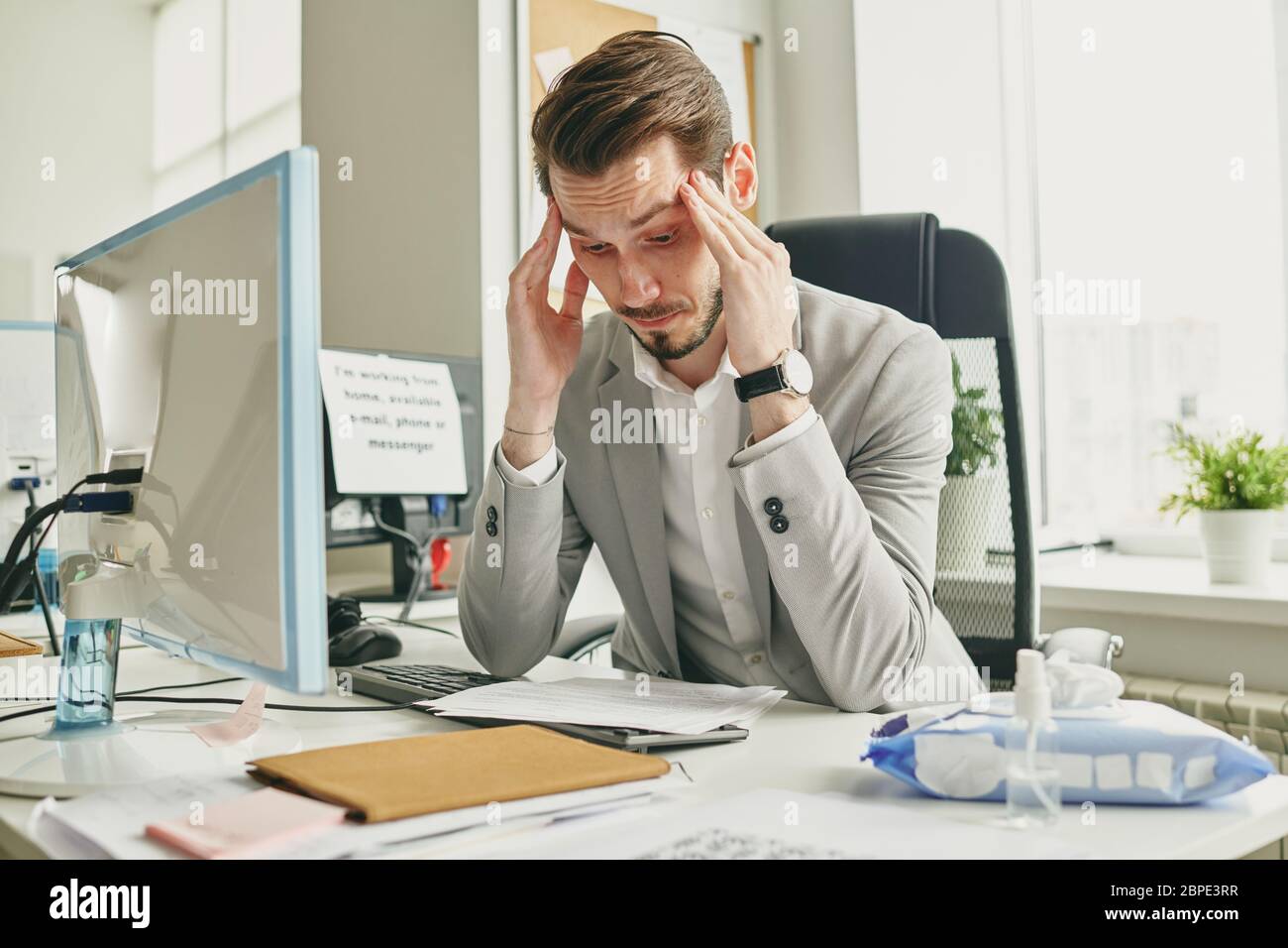 Verwirrt junger Geschäftsmann in Jacke sitzt am Schreibtisch in leerem Büro und massieren Tempel während der Lesung Vereinbarung Stockfoto