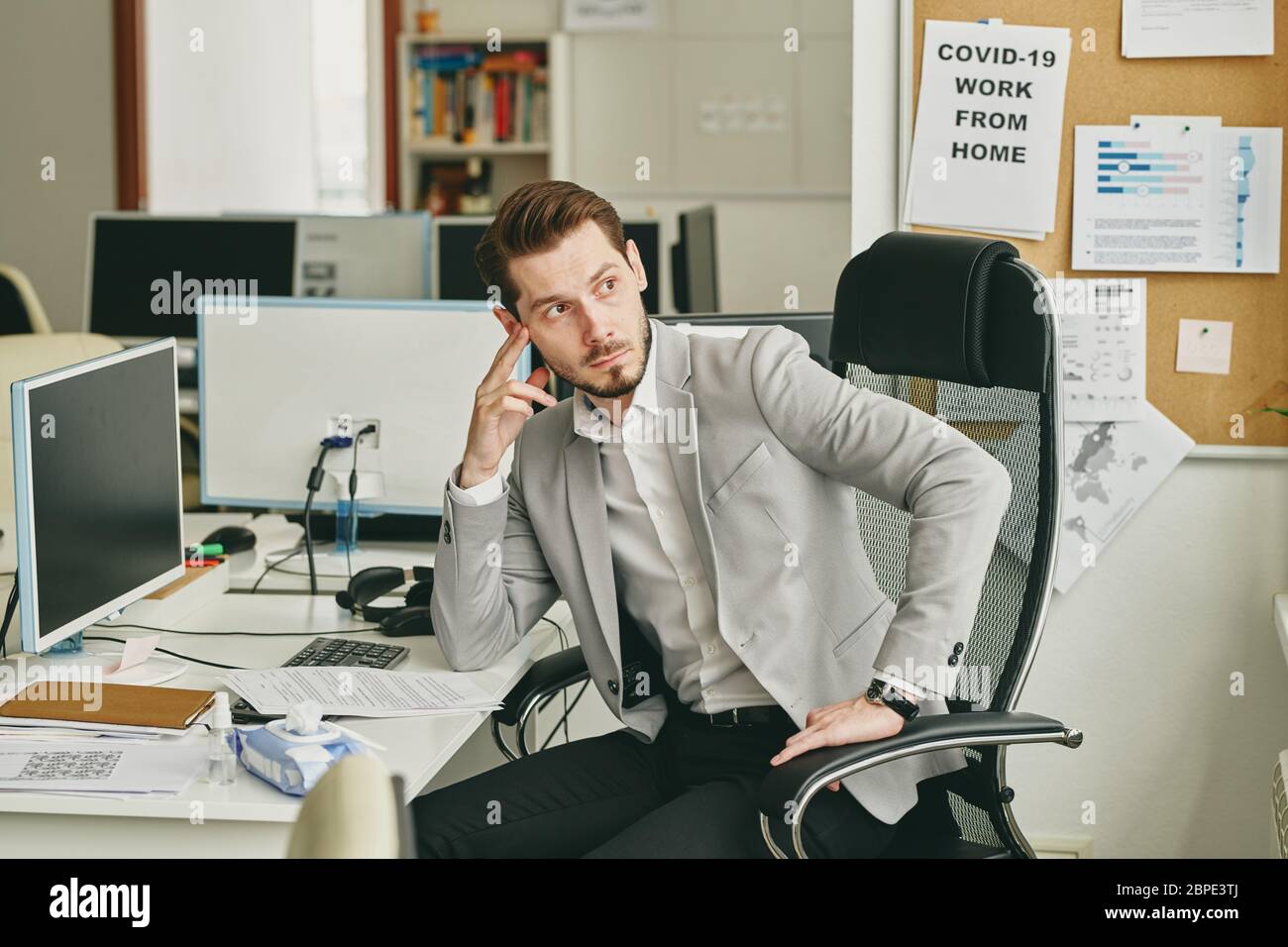Junger bärtiger Geschäftsmann, der sich über Geschäftsprobleme aufregt, sitzt an der Rezeption und schaut während der Quarantäne im leeren Büro weg Stockfoto