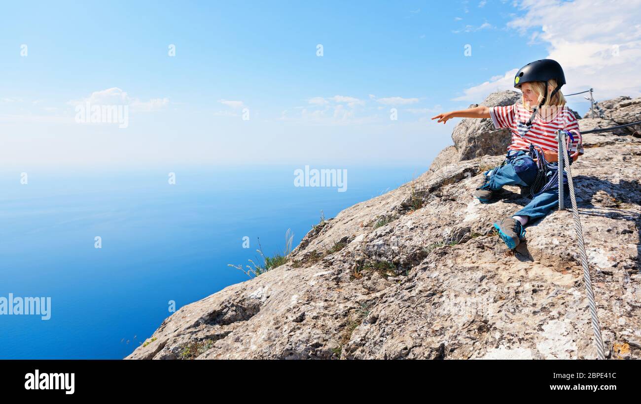 Kleines aktives Kind sitzt auf der Oberseite. Sehen Sie sich die atemberaubende Meereslandschaft an. Familienreise Abenteuer, Wanderaktivität. Klettersteig mit Kindern. Stockfoto