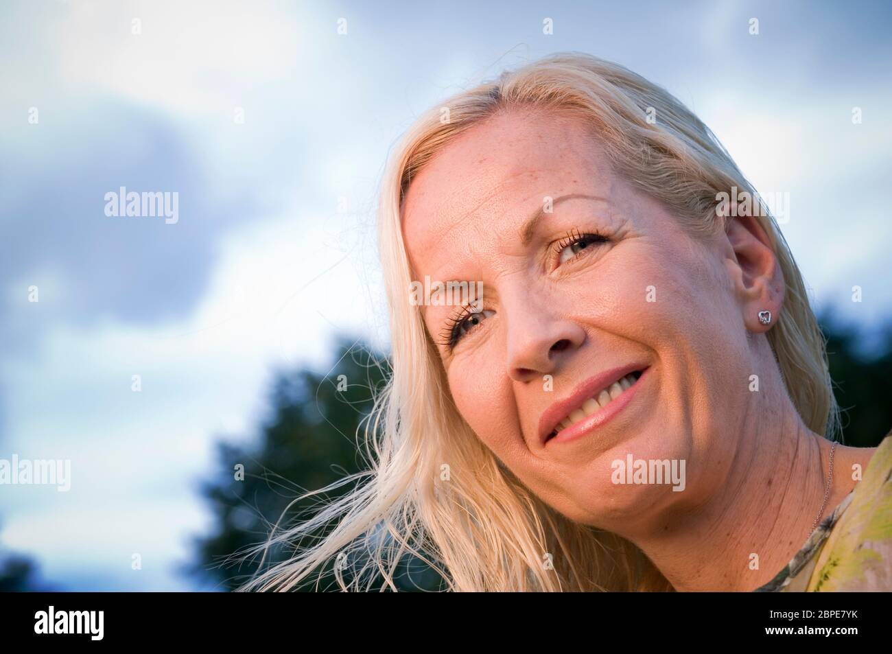 Kopf-Porträt Einer blonden Frau Mittleren Alters in Schrägansicht Freundlichn in Die Kamera lächelnd Stockfoto