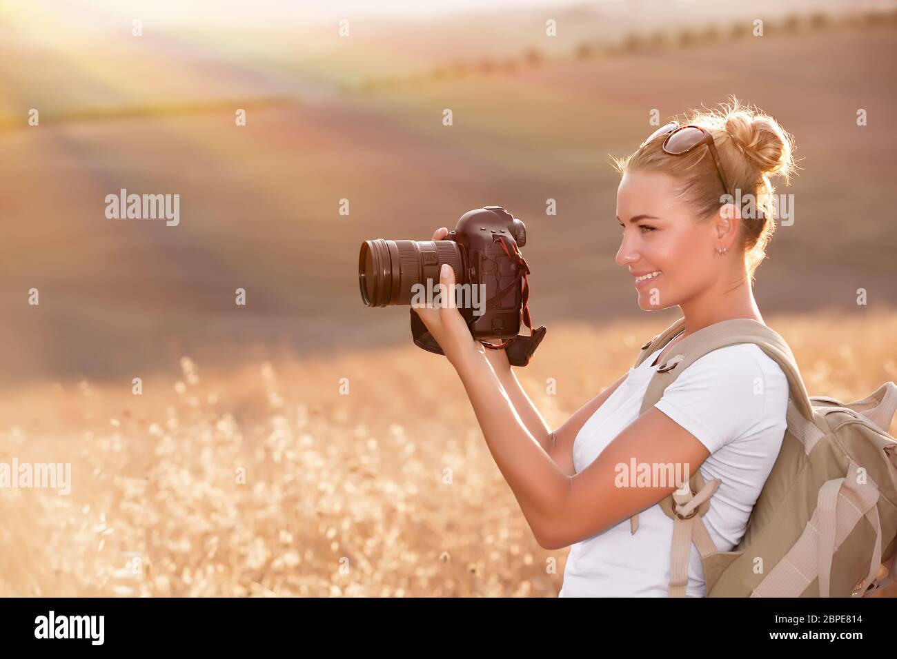 Glückliche Fotograf Herbst Natur genießen, lächelndes Reisenden Mädchen mit Kamera in der Hand fotografieren golden trocken Weizenfeld in Sonnenstrahlen Stockfoto