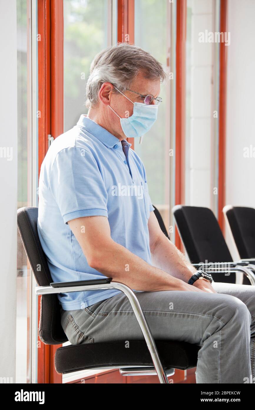 Besucher oder Patient, der wegen des Coronavirus in einem leeren Wartezimmer mit Gesichtsmaske sitzt - Fokus auf das Gesicht Stockfoto