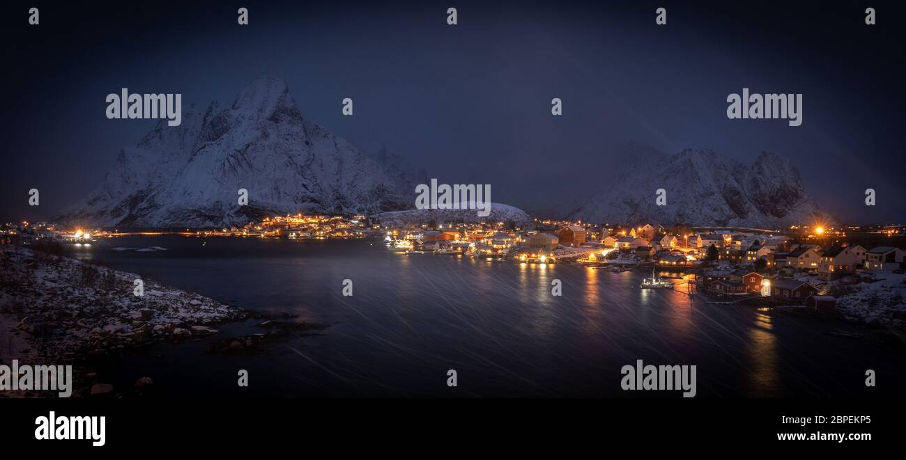 Nachtpanorama des berühmten Fischerdorfes reine, lofoten in schweren Schneesturm. Blizzard und starker Wind am Hafen - im Hintergrund dunkle Berge mit einer bedeckten w Stockfoto
