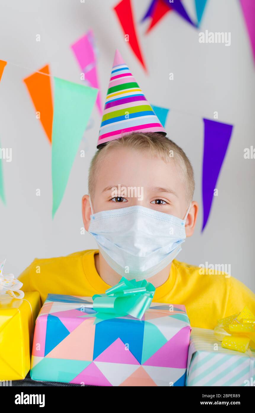 Happy Boy in Medizin Gesichtsmaske und festliche Mütze mit Geschenken in der Hand feiert Geburtstag. Geburtstag allein in Isolation sperren. Soziale Distanz. Stockfoto