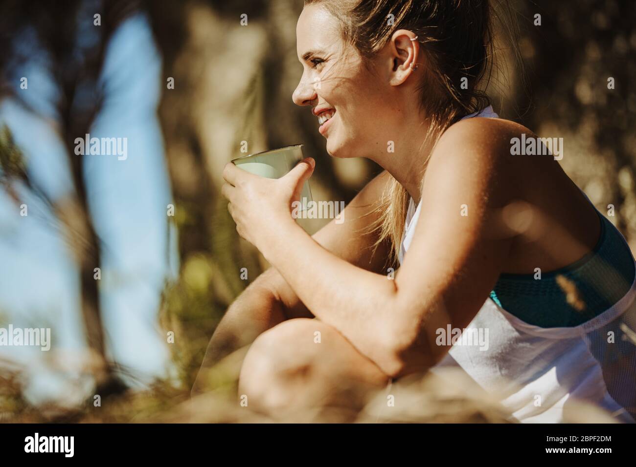 Lächelnde junge Frau, die während des Trekkings Kaffee trinkt. Sportliche Frau, die beim Wandern Ruhe nimmt. Stockfoto
