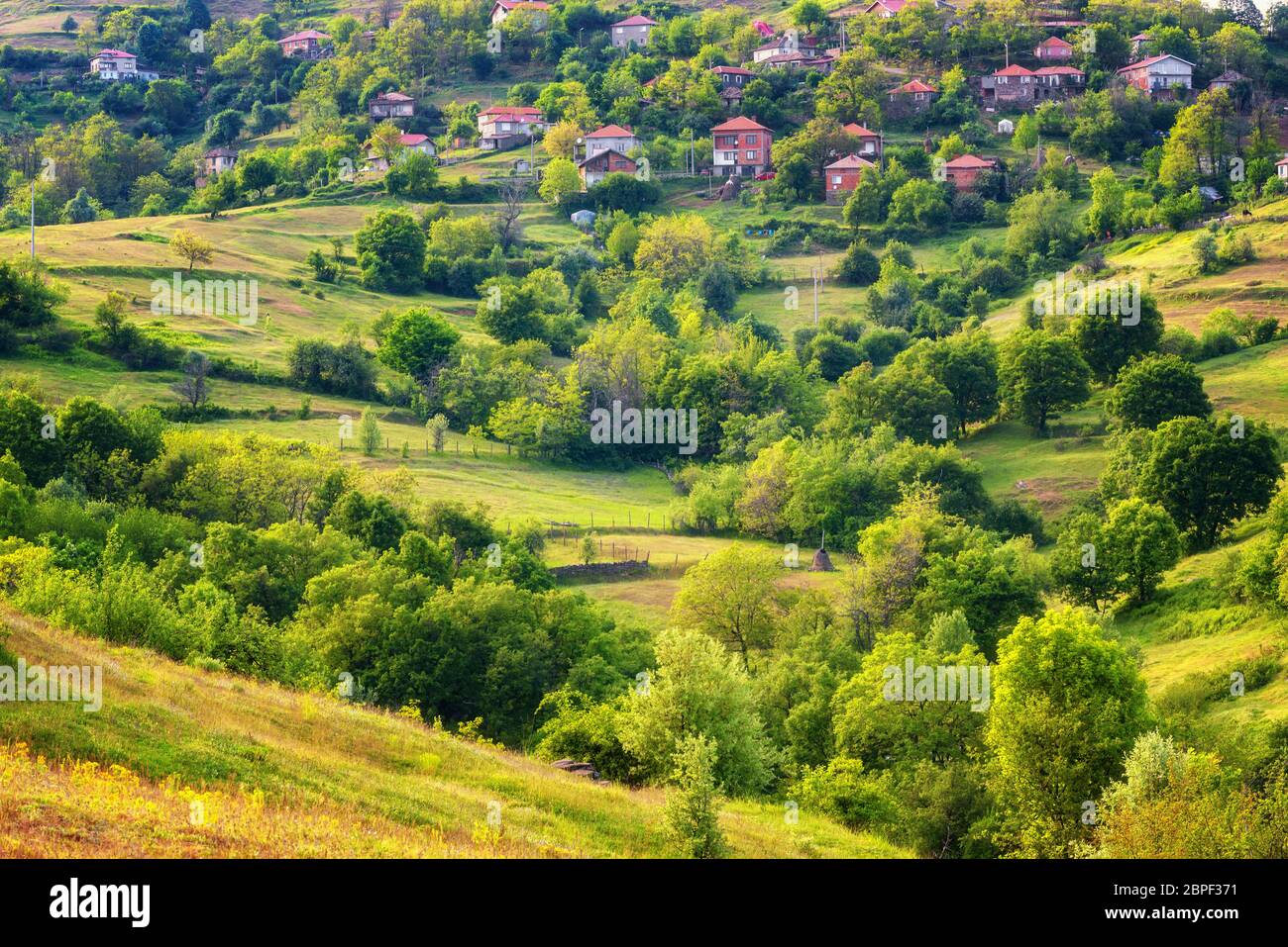 Der Frühling kommt... Erstaunliche Frühling Blick mit einem kleinen Dorf in Rhodopi Gebirge, Bulgarien. Herrliche Landschaft, grüne Felder, kleine Häuser. Stockfoto