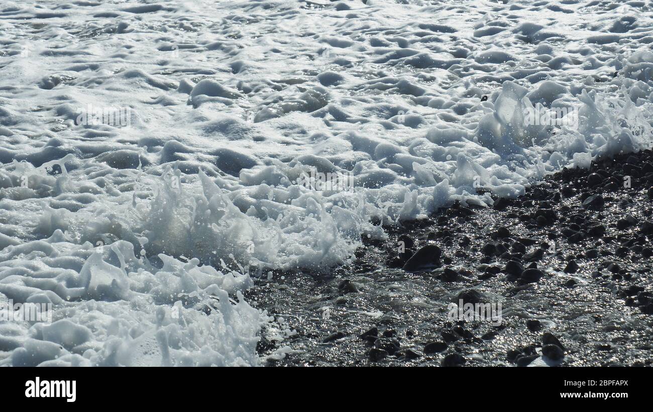 Der Rand der Brandung bricht an einem typischen neuseeländischen Westküstenstrand, einem Ufer mit kleinen Felsen Stockfoto