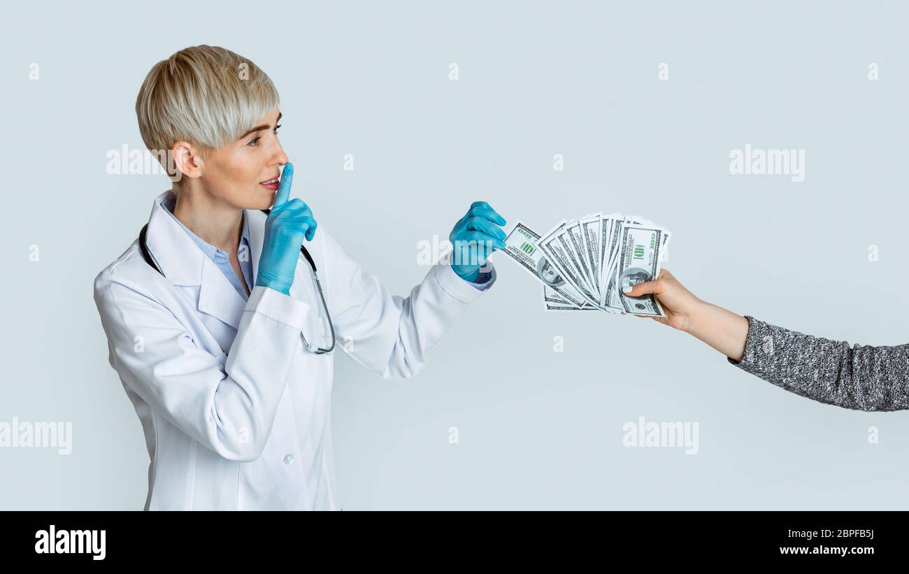Frau Ärztin in medizinischen Handschuhen nimmt Geld von den Händen des Patienten und macht Zeichen der Stille Stockfoto