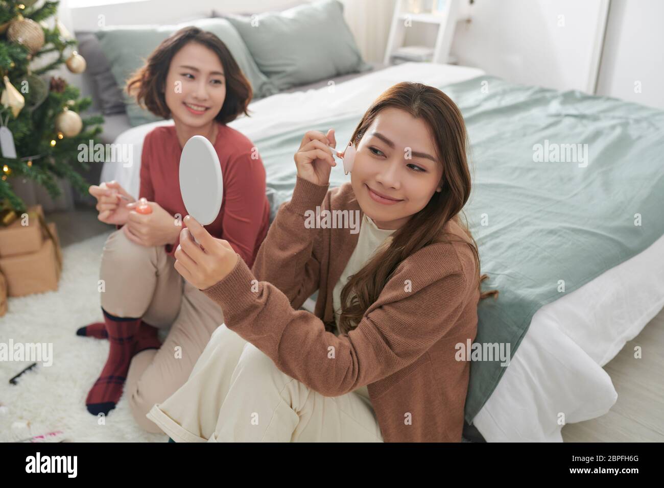 Zwei Frauen zusammen auf einer Pflegebehandlung mit Gesichtsrollen für die Hautstraffung. Stockfoto