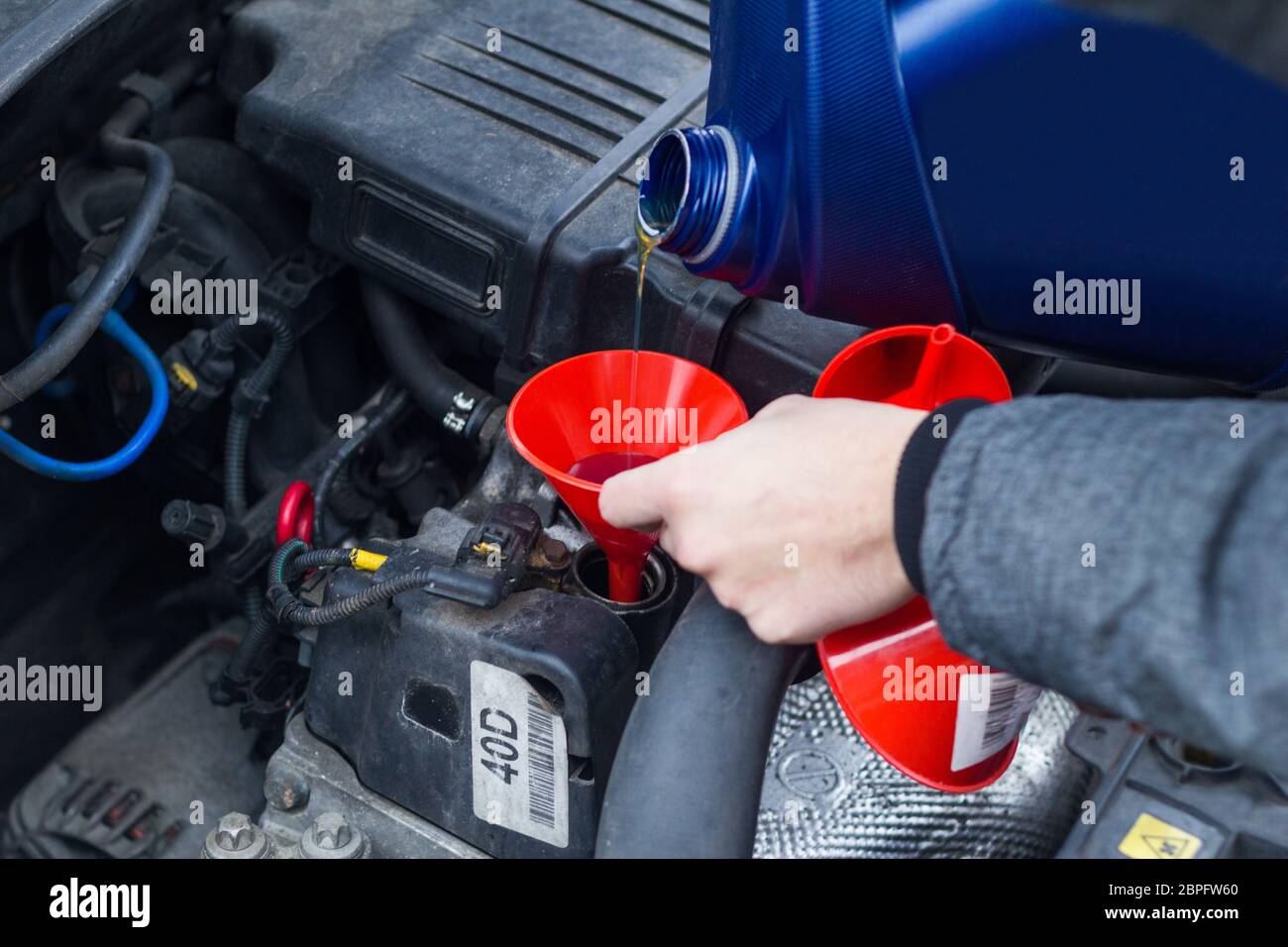 Man füllt das Motoröl in einem Auto mit einem blauen Behälter mit einem roten Trichter. Mechatronik-Ölstandsexperte E-Mobilität Stockfoto