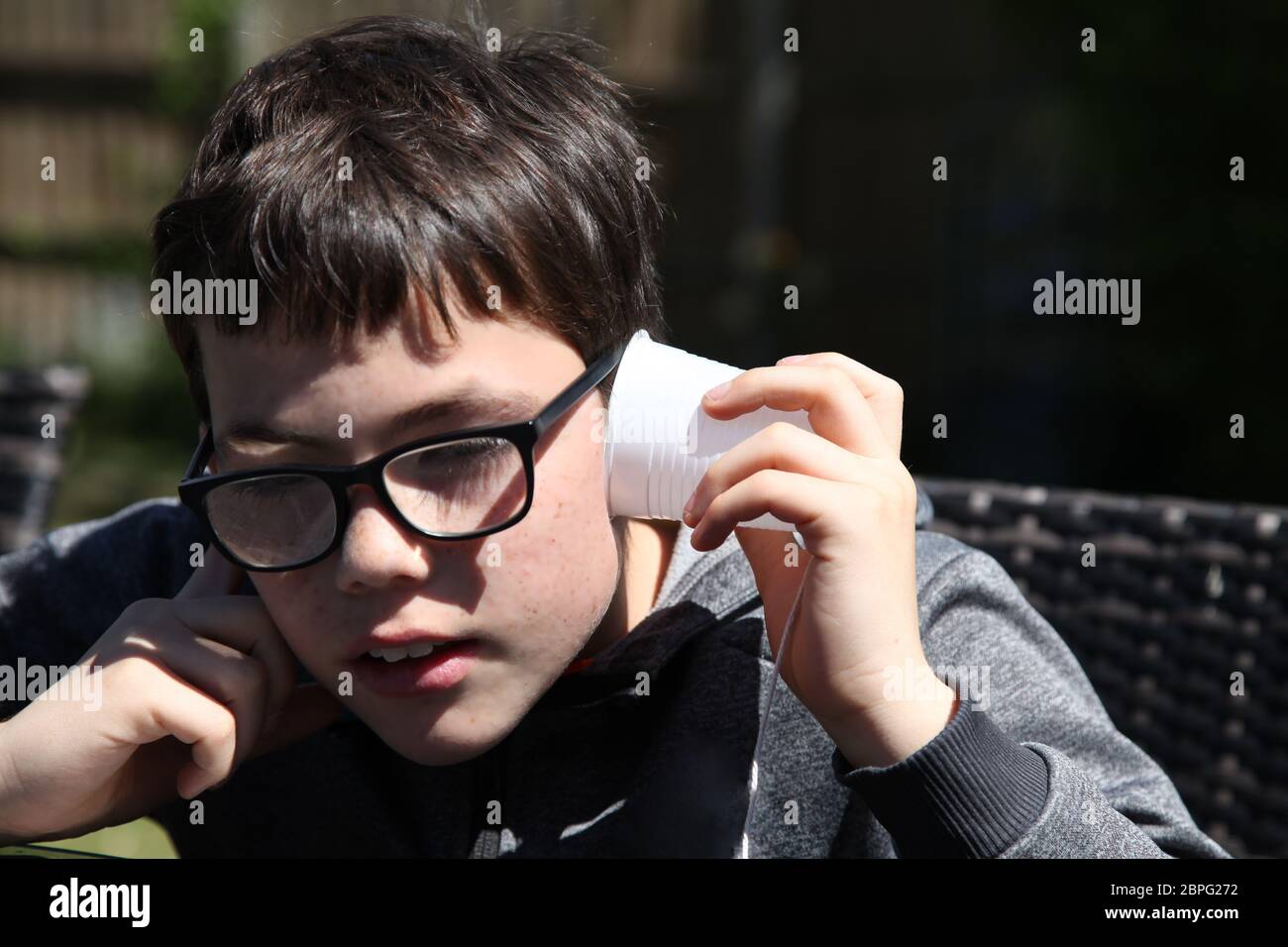 Junge hört mit einem Papptassentelefon aus Plastikbechern und Schnur experimentiert die Wissenschaft mit Schallwellen und Vibrationen Stockfoto