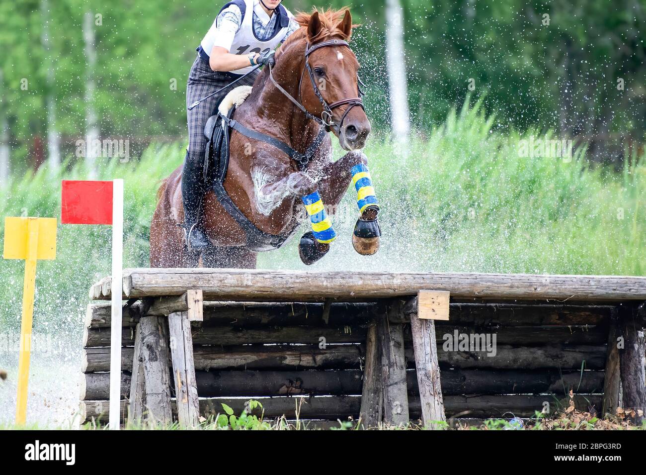 Vielseitigkeitsreiten: Reiter springen über einen Holzzaun Wasserhindernis in Splash Stockfoto