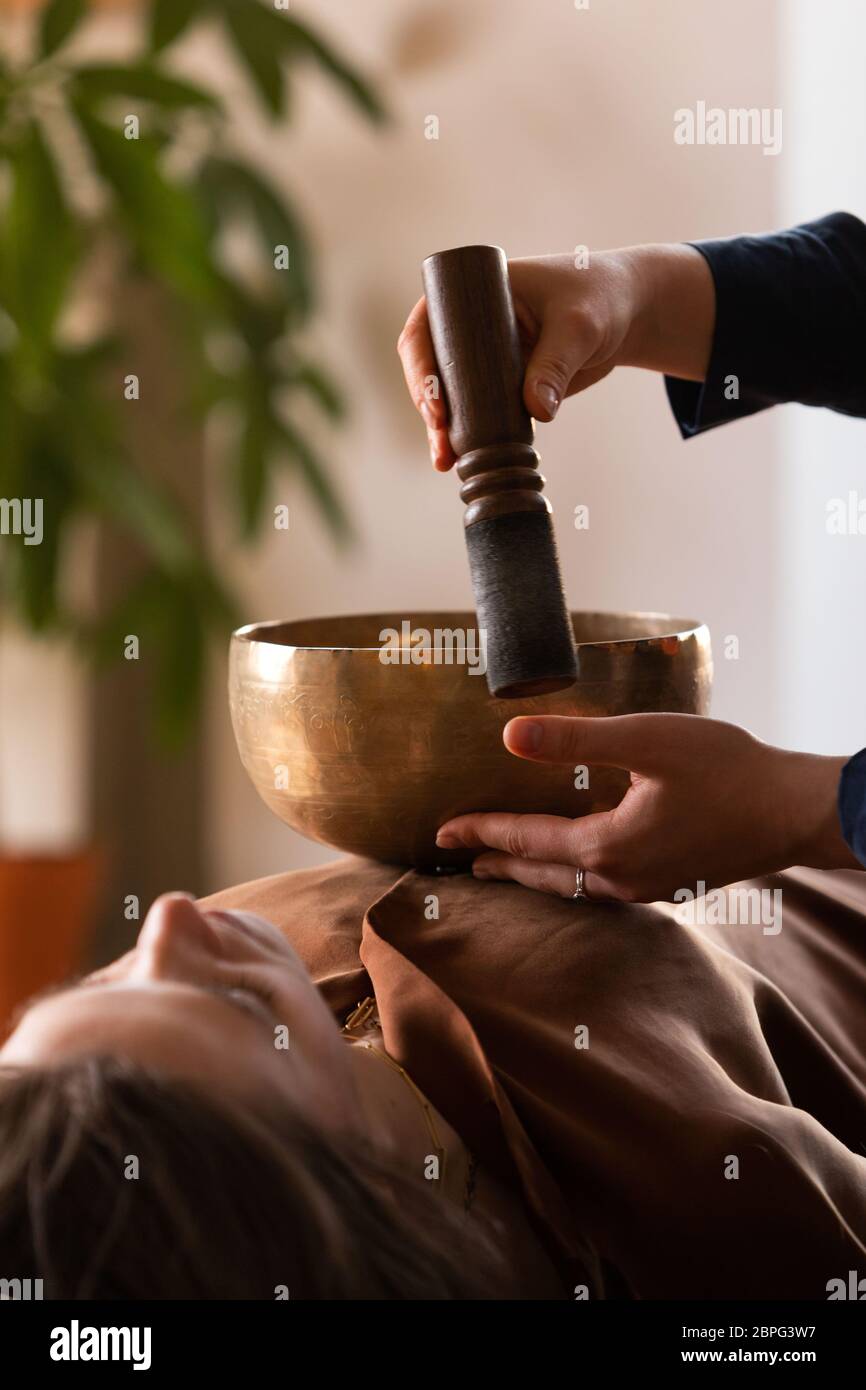 Frau macht entspannende Massage, Meditation, Klangtherapie mit tibetischen Klangschalen. Stressabbau. Selektiver Fokus. Ansicht von unten. Stockfoto