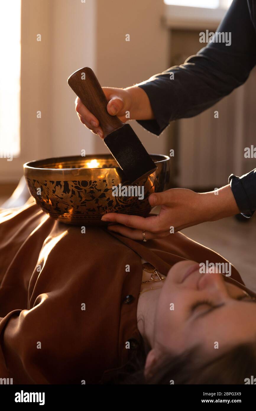 Frau macht entspannende Massage, Meditation, Klangtherapie mit tibetischen Klangschalen. Stressabbau. Selektiver Fokus. Ansicht von unten. Stockfoto
