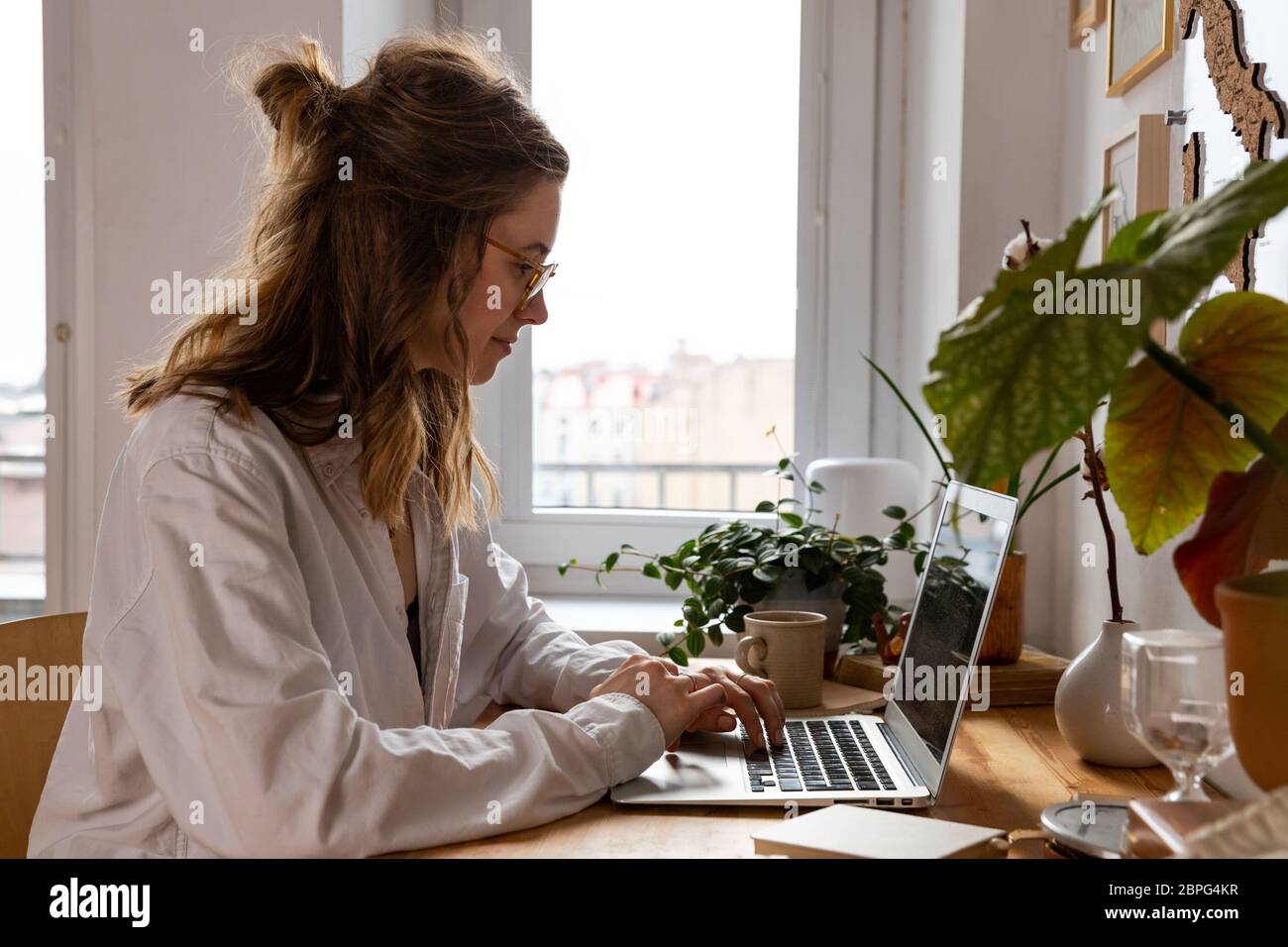 Junge Frau freiberufliche/Designer arbeitet am Computer aus dem Home Office während der Selbstisolierung durch Coronavirus. Gemütlicher Arbeitsplatz umgeben von Pflanzen. Re Stockfoto