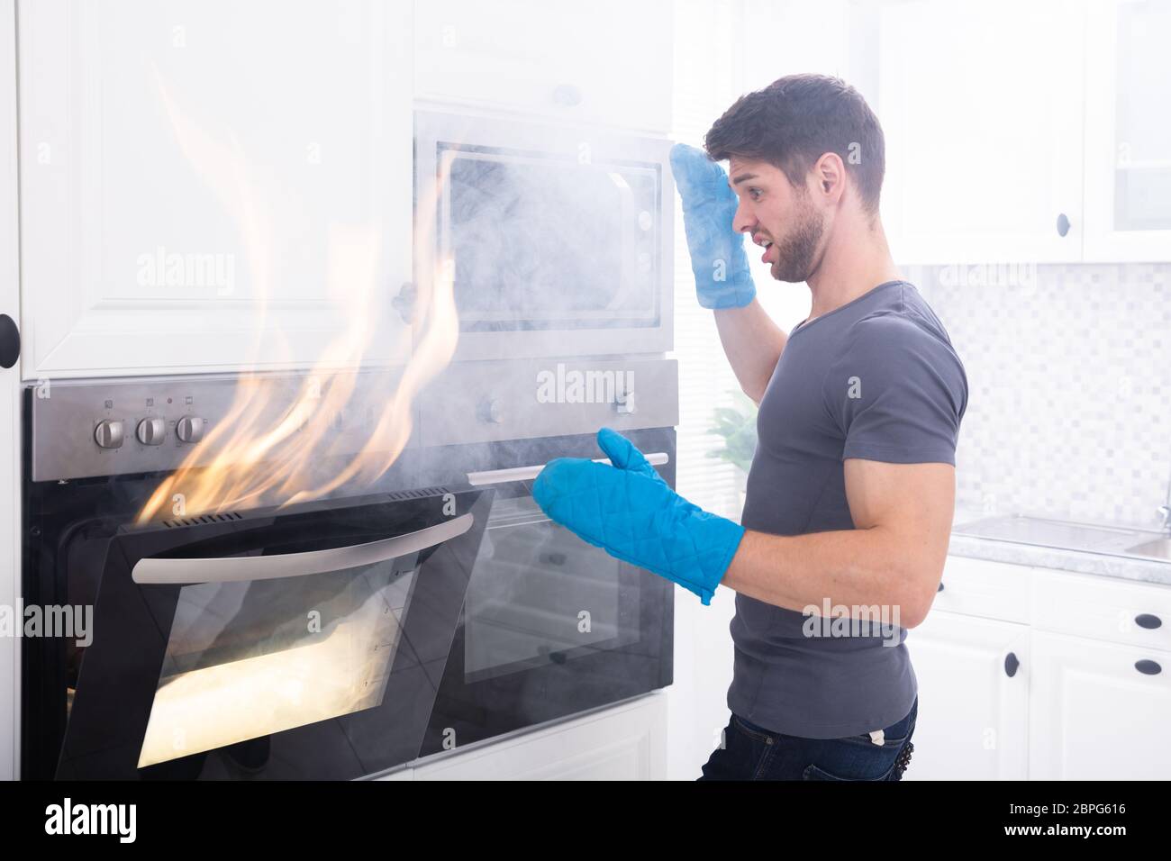 Angst junger Mann auf der Suche nach Feuer kommen aus dem Ofen in der Küche Stockfoto