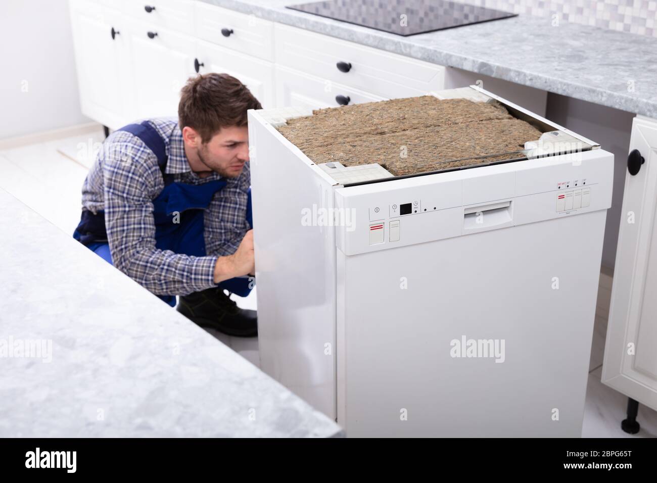 Junge männliche Techniker Reparatur Geschirrspüler in der Küche Stockfoto