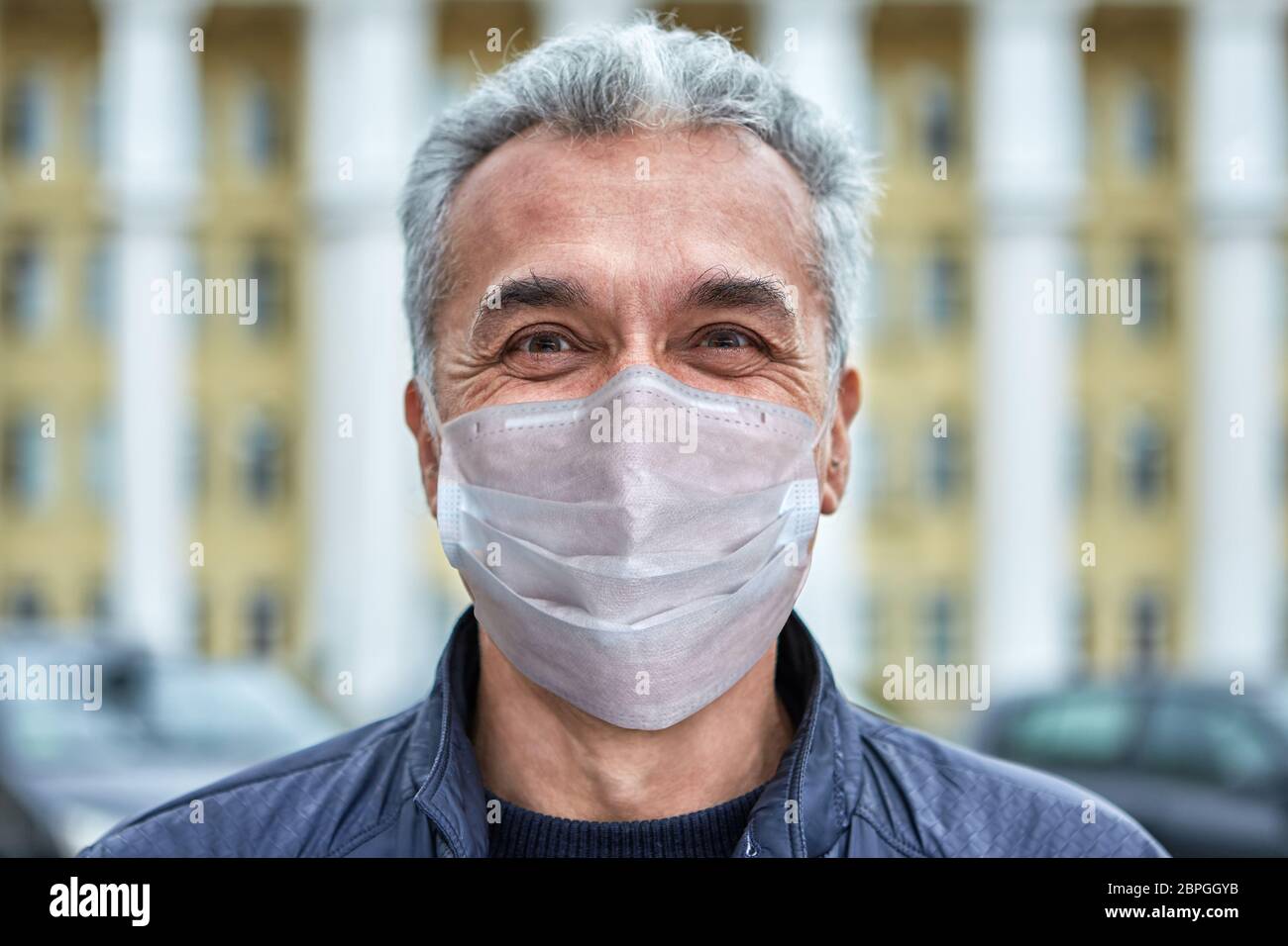 Lächelnder weißer kaukasischer Mann in einer Einweg-Schutzmaske in einer Periode des Coronavirus Covid-19 Pandemie geht auf der Straße. Stockfoto