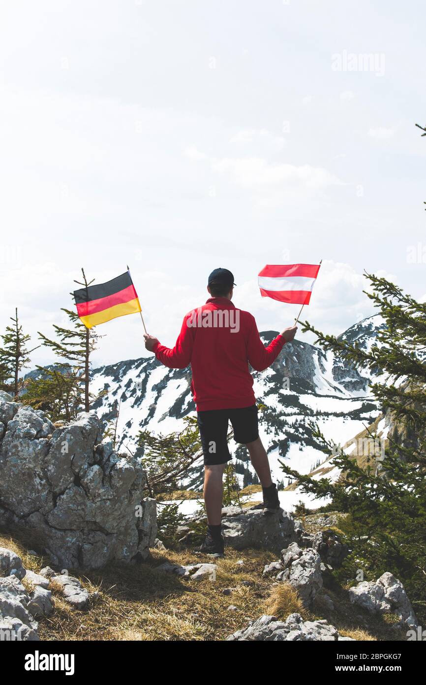 Männliche Wanderer mit roten Pullover hält eine deutsche Flagge in den Bergen Stockfoto
