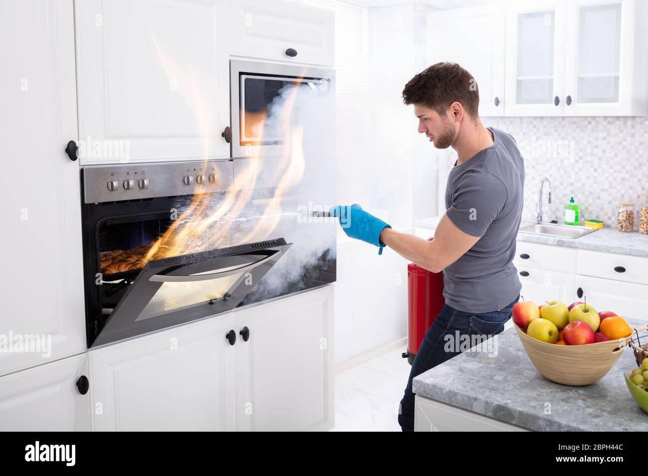Mann mit Feuerlöscher zu stoppen Feuer kommen aus dem Ofen in der Küche Stockfoto