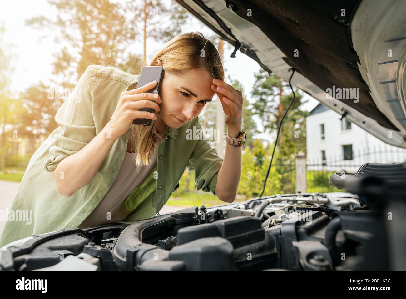 Frau, die auf einen kaputten Motor schaut und am Telefon spricht Stockfoto