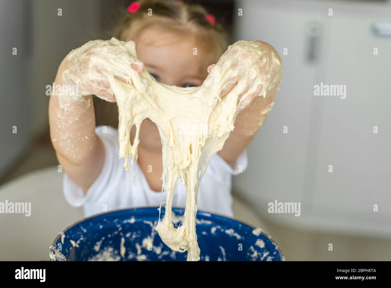 3-4 Jahre altes Mädchen knetet Hefeteig in einer blauen Pfanne, Hände Nahaufnahme. Familienfreizeit Stockfoto