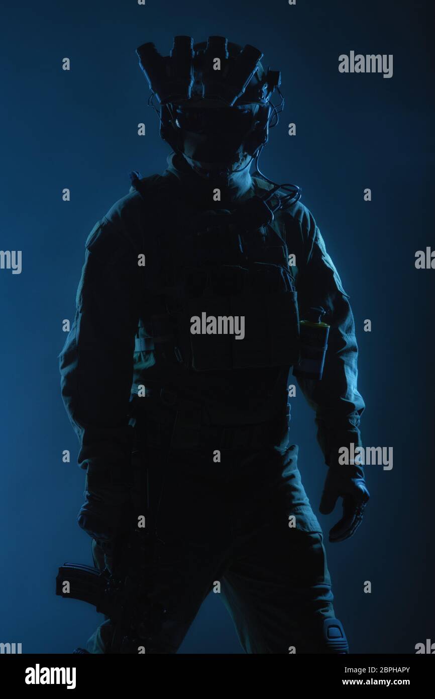 Army Special forces Soldat in taktische Munition, Nachtsichtgerät auf Helm, stehend mit abgesenktem service Gewehr in der Hand Low Key, Rückansicht, Stu Stockfoto