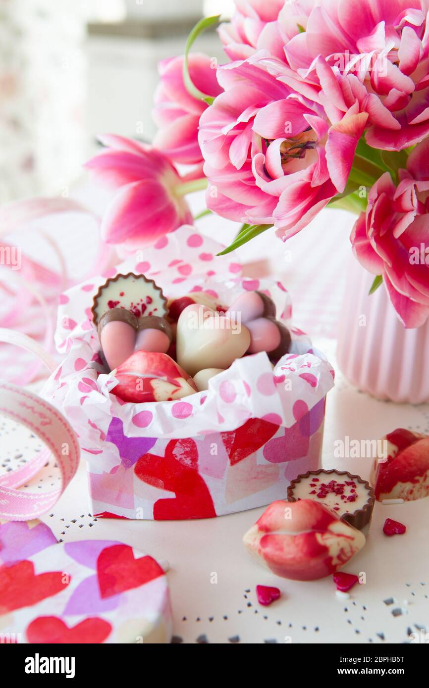 Leckere Süßigkeiten in Form eines Herzens und frisches rosa Tulpen Stockfoto