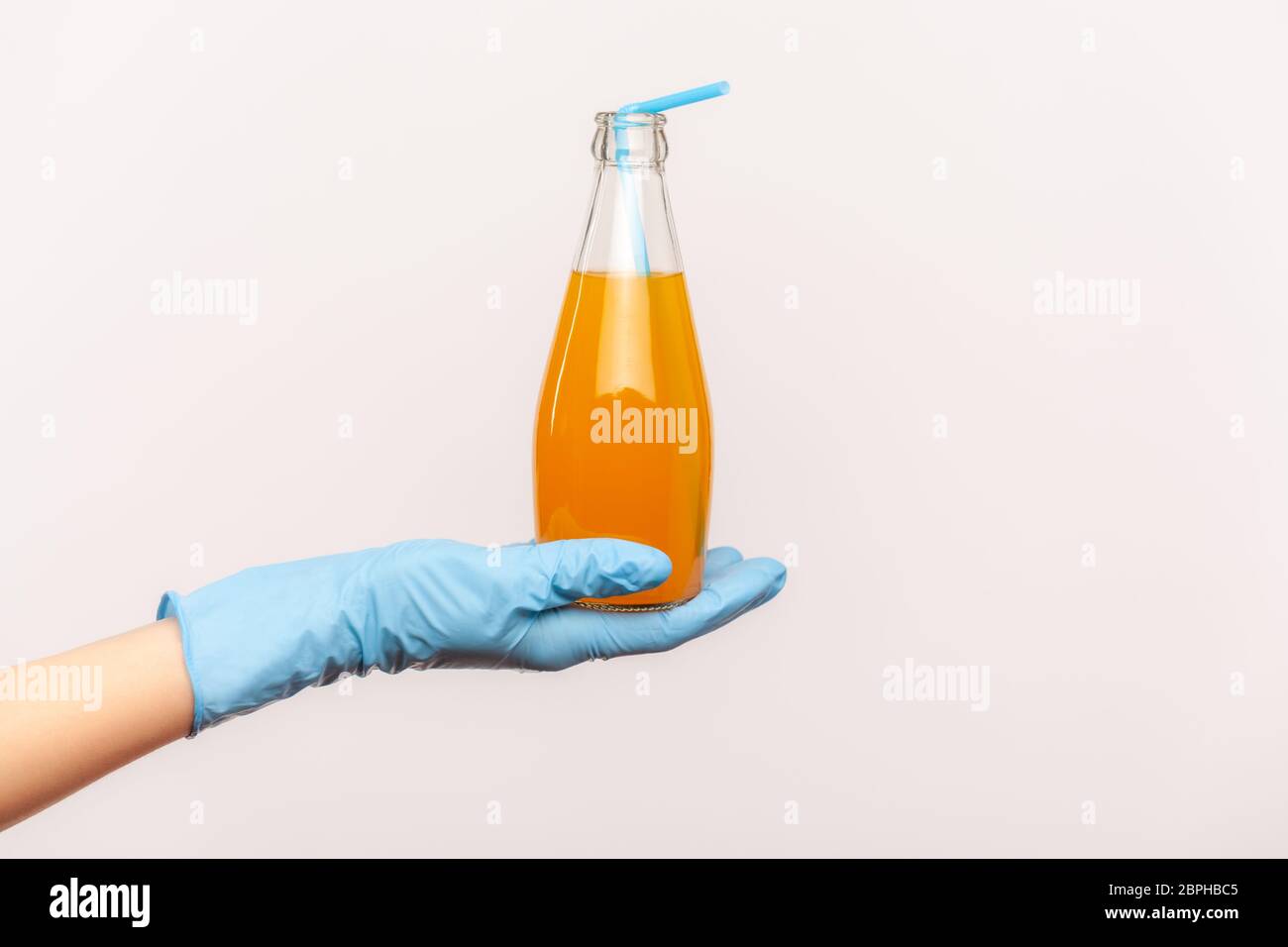 Profil Seitenansicht Nahaufnahme der menschlichen Hand in blauen chirurgischen Handschuhen halten Flasche Orangengetränk. Orangensaft oder Cocktail in der Hand. Safe Food Konzept. i Stockfoto