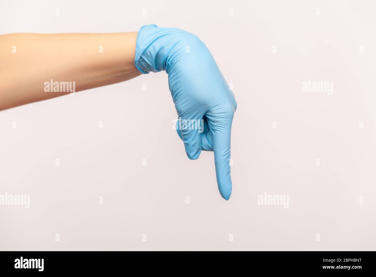 Profil Seitenansicht Nahaufnahme der menschlichen Hand in blauen chirurgischen Handschuhen zeigen oder zeigen mit dem Finger nach unten. Indoor, Studio-Aufnahme, isoliert auf grauem Hintergrund Stockfoto