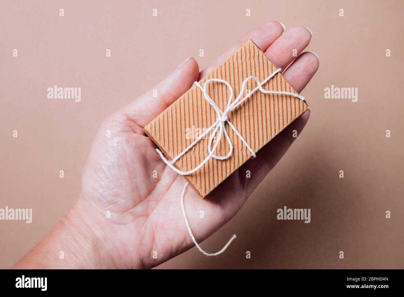 Niedliche kleine gewellte Geschenkbox mit Naturschnur in weiblicher Hand. Stockfoto