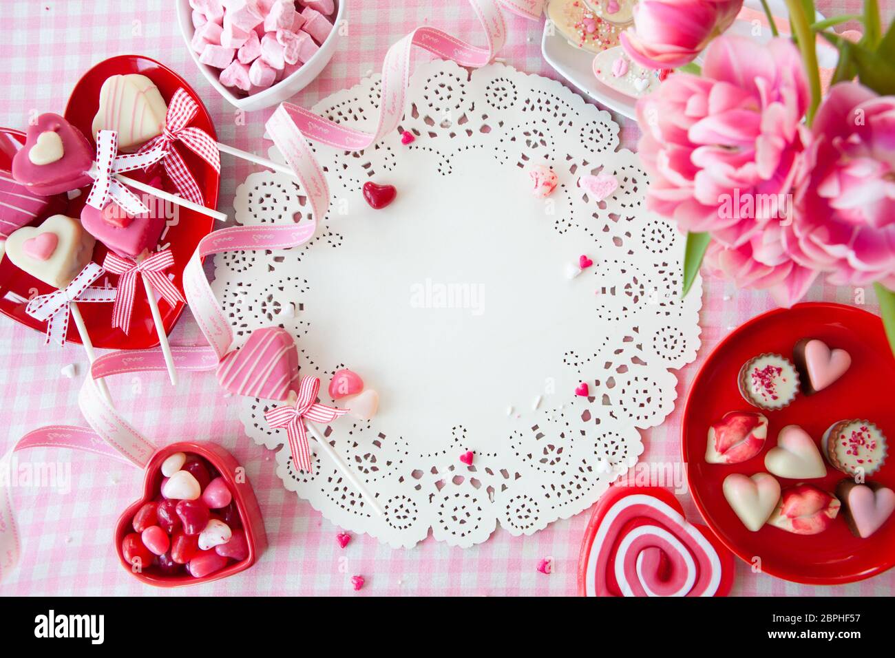Leckere Süßigkeiten in Form eines Herzens und frisches rosa Tulpen Stockfoto
