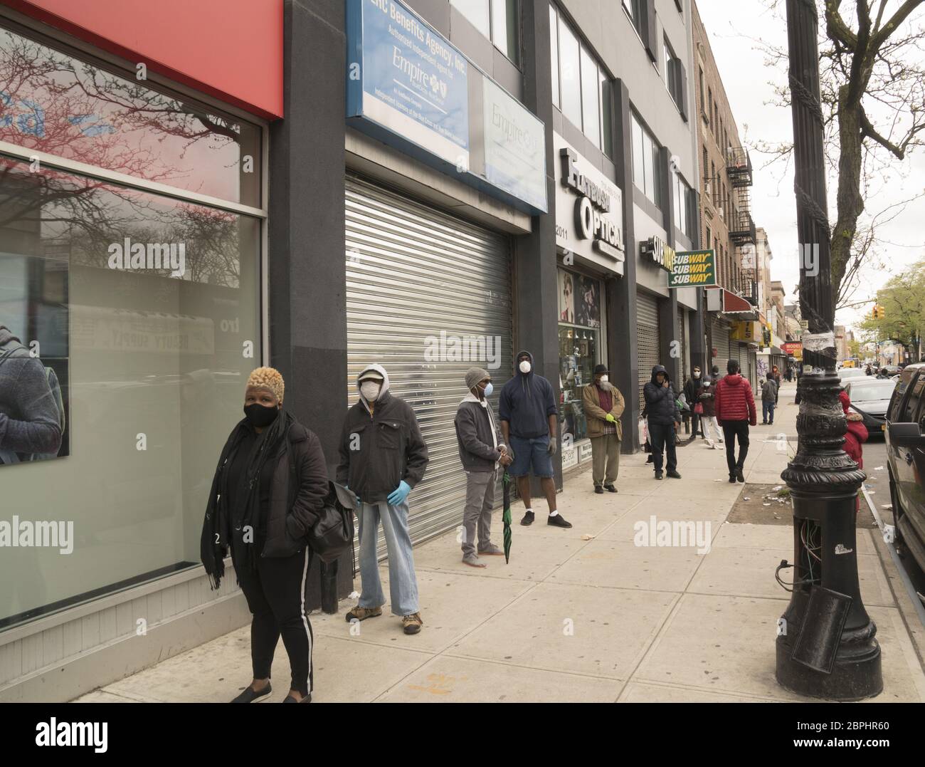 Menschen, die sich auf dem Bürgersteig distanzieren, während sie darauf warten, eine Bank entlang der Church Avenue in Brooklyn, New York, zu betreten. Stockfoto