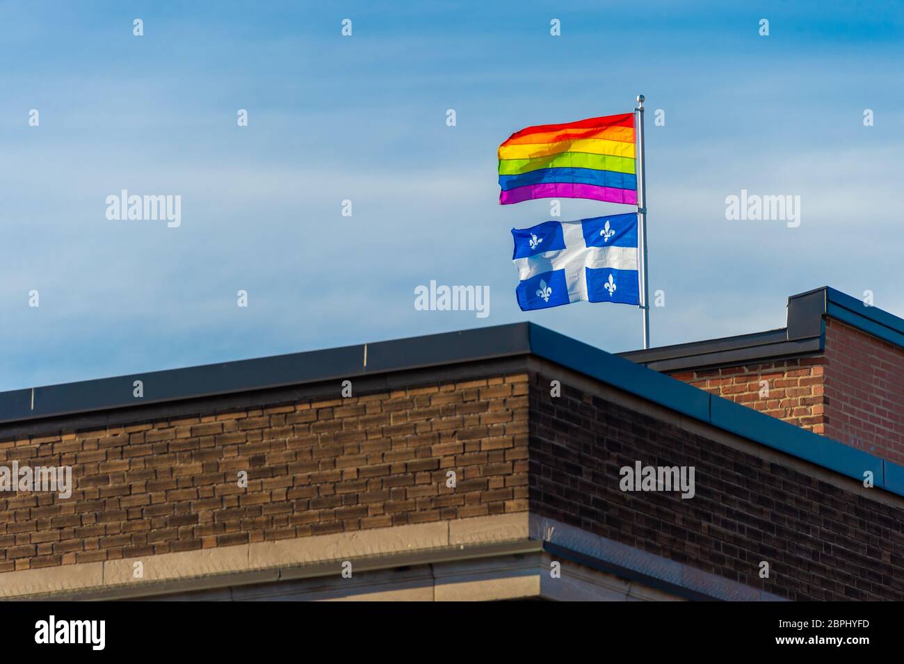 Schwule Regenbogenfahne und Quebecer Flagge winken im Wind auf dem Dach eines Gebäudes in Montreal, Kanada Stockfoto