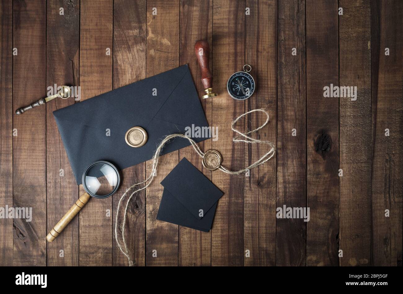 Vintage Schreibwaren mockup. Foto von leeren schwarzen Umschlag, Siegellack, Stempel, Lupe, Kompass und Löffel auf Holz- Hintergrund. Vorlage für das Inverkehrbringen Stockfoto
