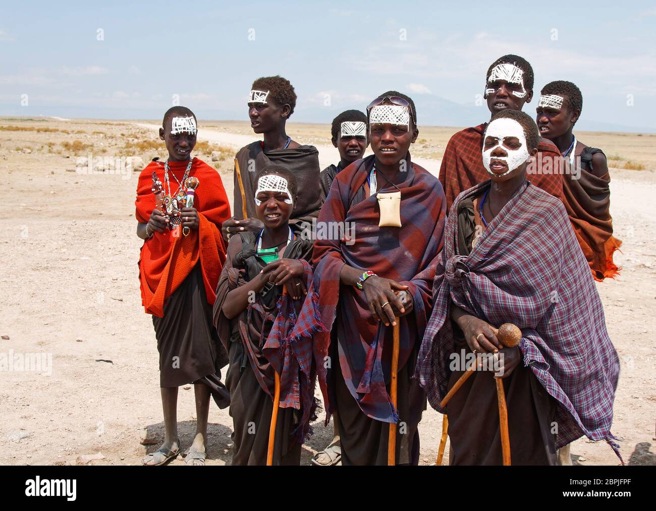 Acht Maasai-Jungen, weiße Farbe auf Gesichtern, Roben, Spazierstöcke, Posen, karges Land, Ureinwohner; Tansania, Afrika Stockfoto