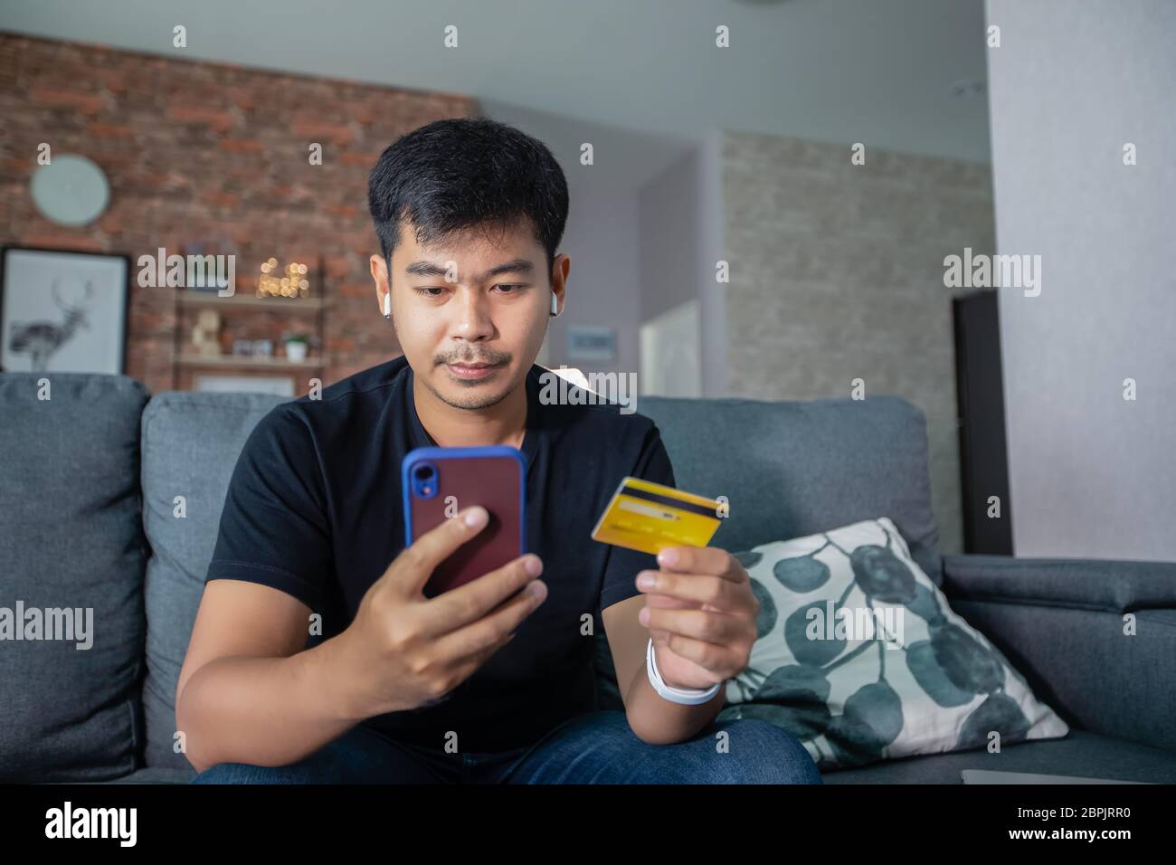 Asiatischer Mann hält Kreditkarte und verwendet Smartphone-Shopping online zu Hause.Online-Shopping, E-Commerce, Internet-Banking, Geld ausgeben, arbeiten Stockfoto
