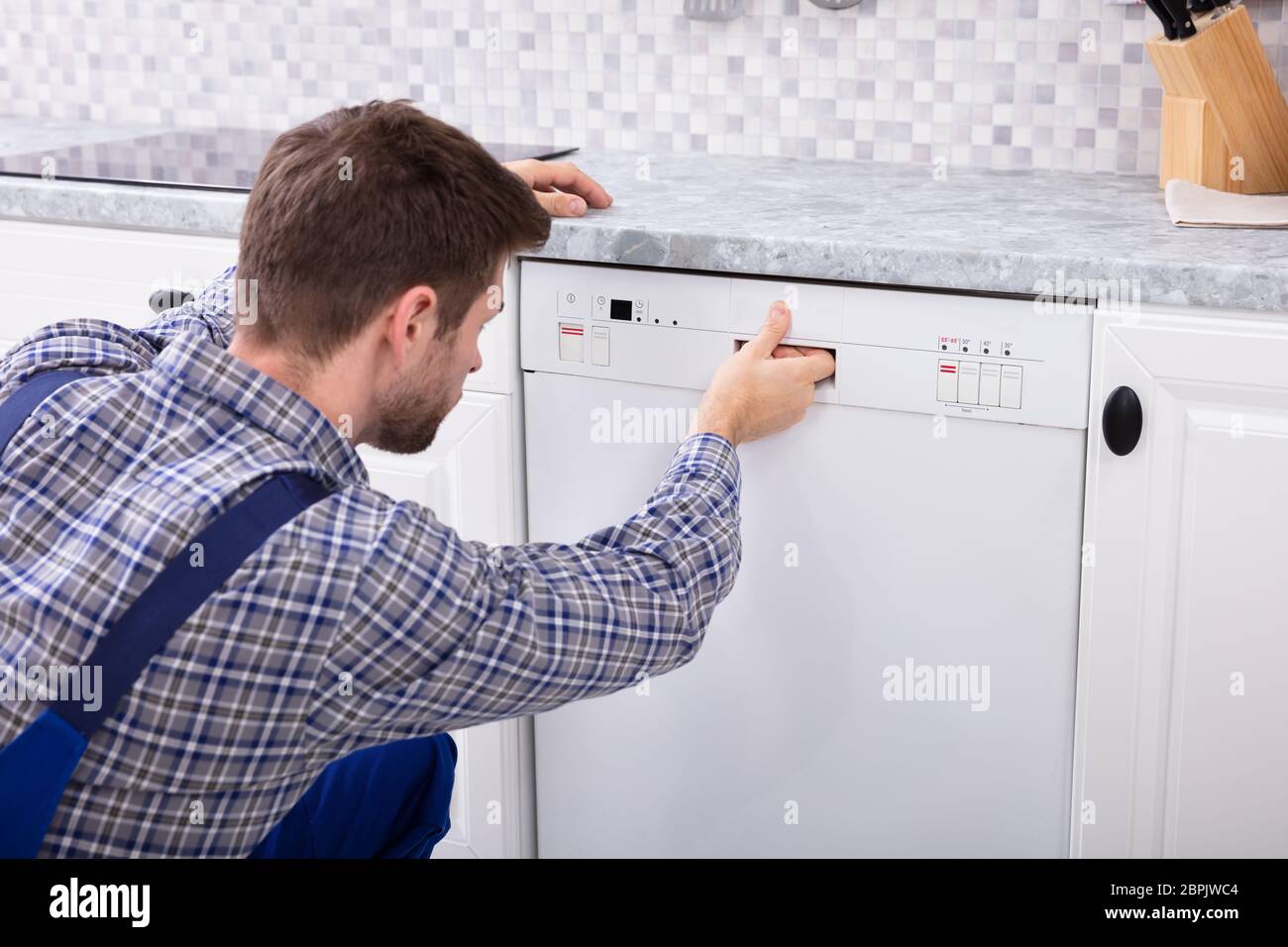 Junge Offiziere durch Drücken der Taste der Spülmaschine in der Küche Stockfoto