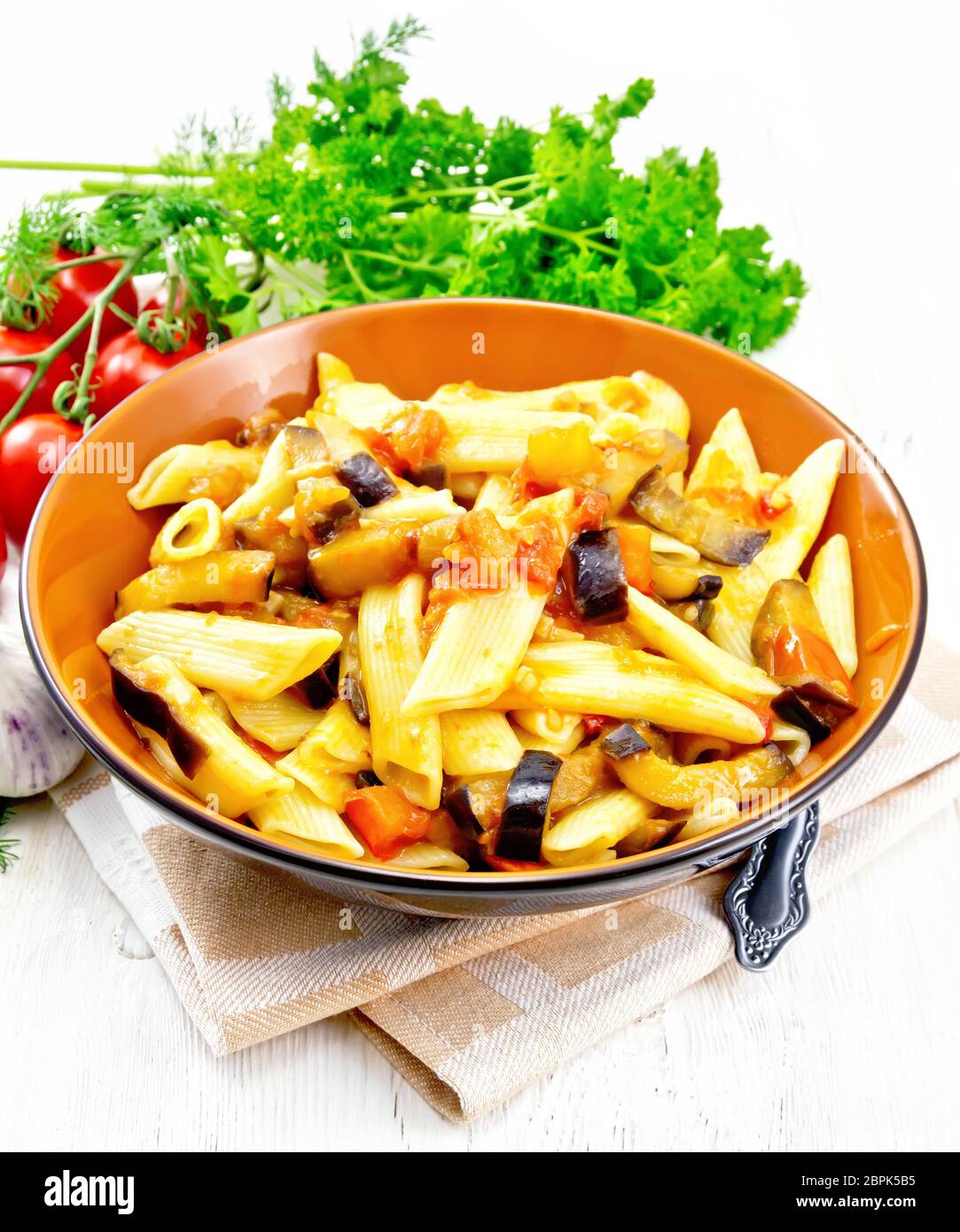 Penne Pasta mit Auberginen und Tomaten in eine Schüssel geben und auf Küchenpapier, Gabel, Knoblauch und Petersilie auf Light Board Hintergrund Stockfoto