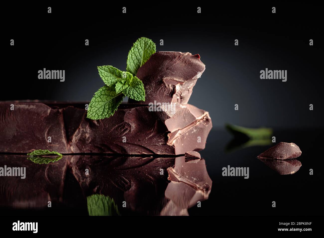 Großes Stück Bitterschokolade mit Minze auf schwarzem reflektierendem Hintergrund. Kopierbereich. Stockfoto