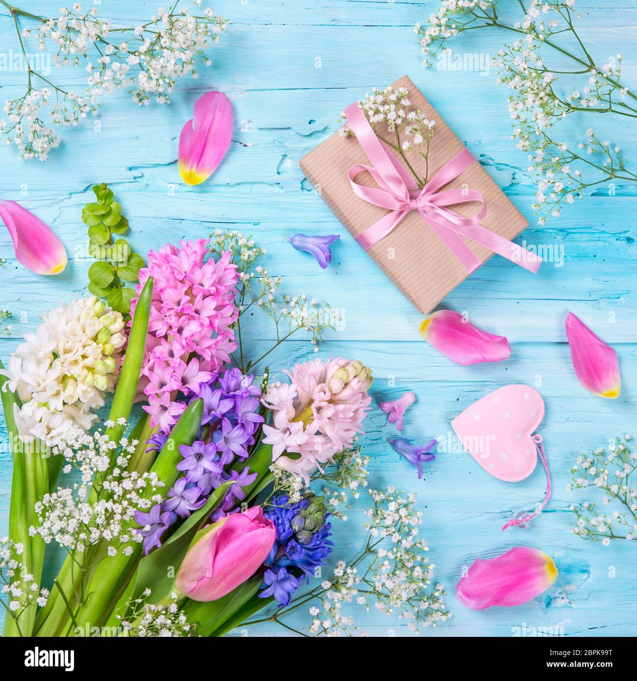 Pastellfarbene Blumen und eine Geschenkbox auf blauem Hintergrund Stockfoto