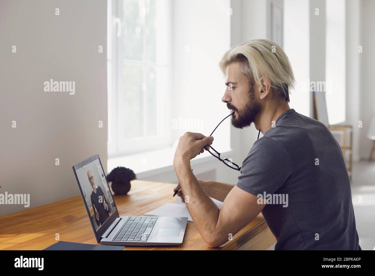 Online-Schulungen. Junger Mann, der einen Videoanruf von einem Dozenten der Universität mit einem Laptop ansieht, während er im Wohnzimmer sitzt. Stockfoto
