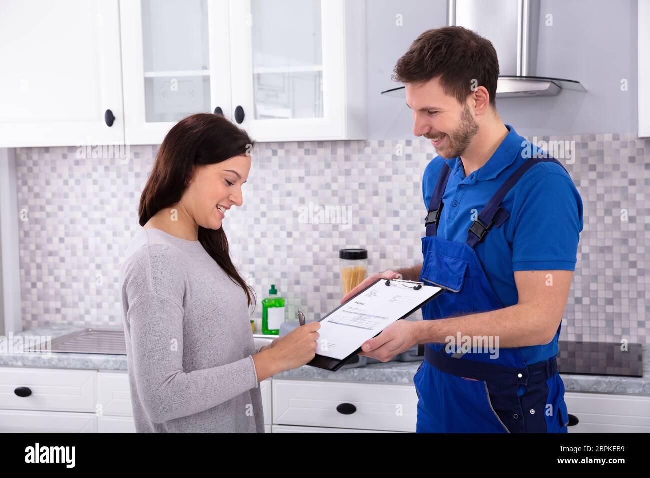 Glückliche junge männliche Klempner bei Frau Unterzeichnung Rechnung in der Küche Stockfoto