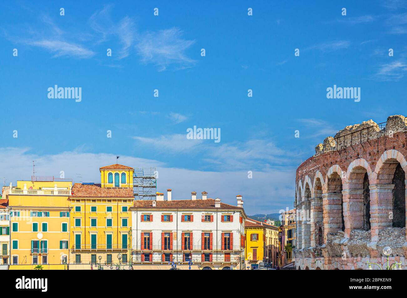 Die Verona Arena Kalksteinwände mit Bogenfenstern und alten bunten bunten Gebäuden auf der Piazza Bra Platz in Verona Altstadt, blauer Himmel Hintergrund, Region Venetien, Norditalien Stockfoto