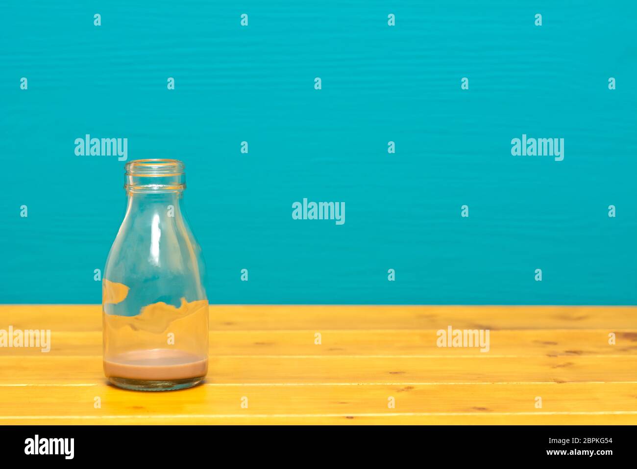 Ein Drittel pint Glas Milch Flasche mit Abschaum der Schokolade Milchshake, auf einen hölzernen Tisch gegen einen hellen Teal gemalten Hintergrund Stockfoto