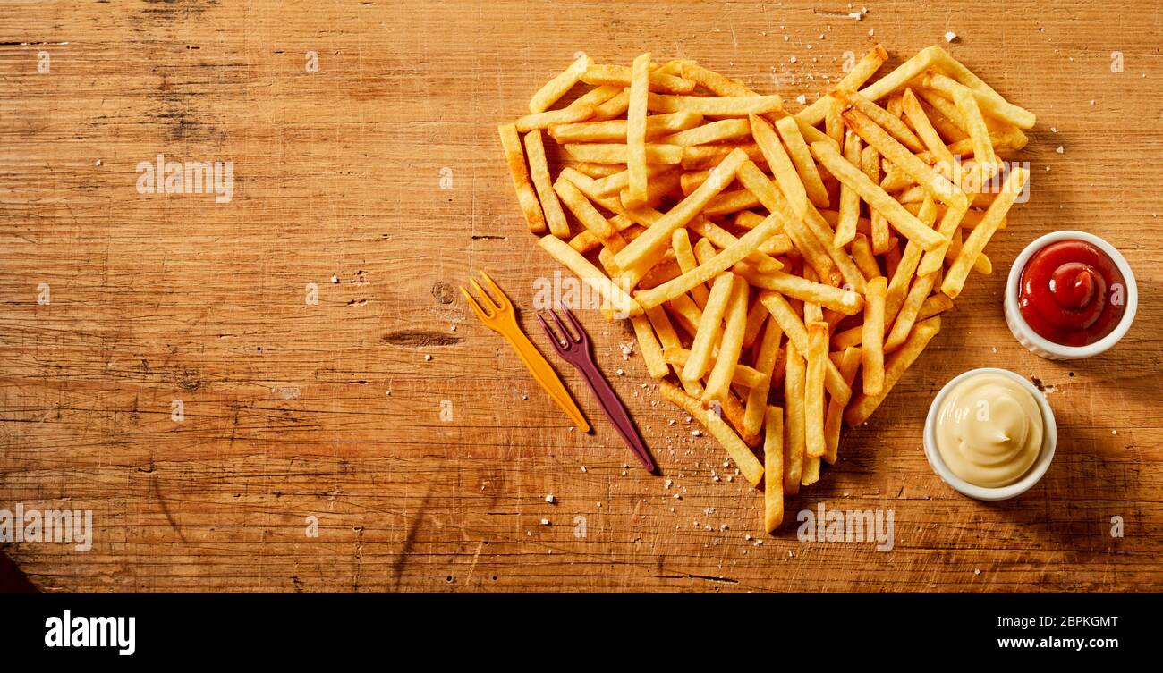 In Herzform dienen oder frittierten Kartoffelchips, Pommes frites oder Pommes frites auf rustikalem Holz mit Senf und Mayonnaise mischen und Tomatensauce vie Stockfoto