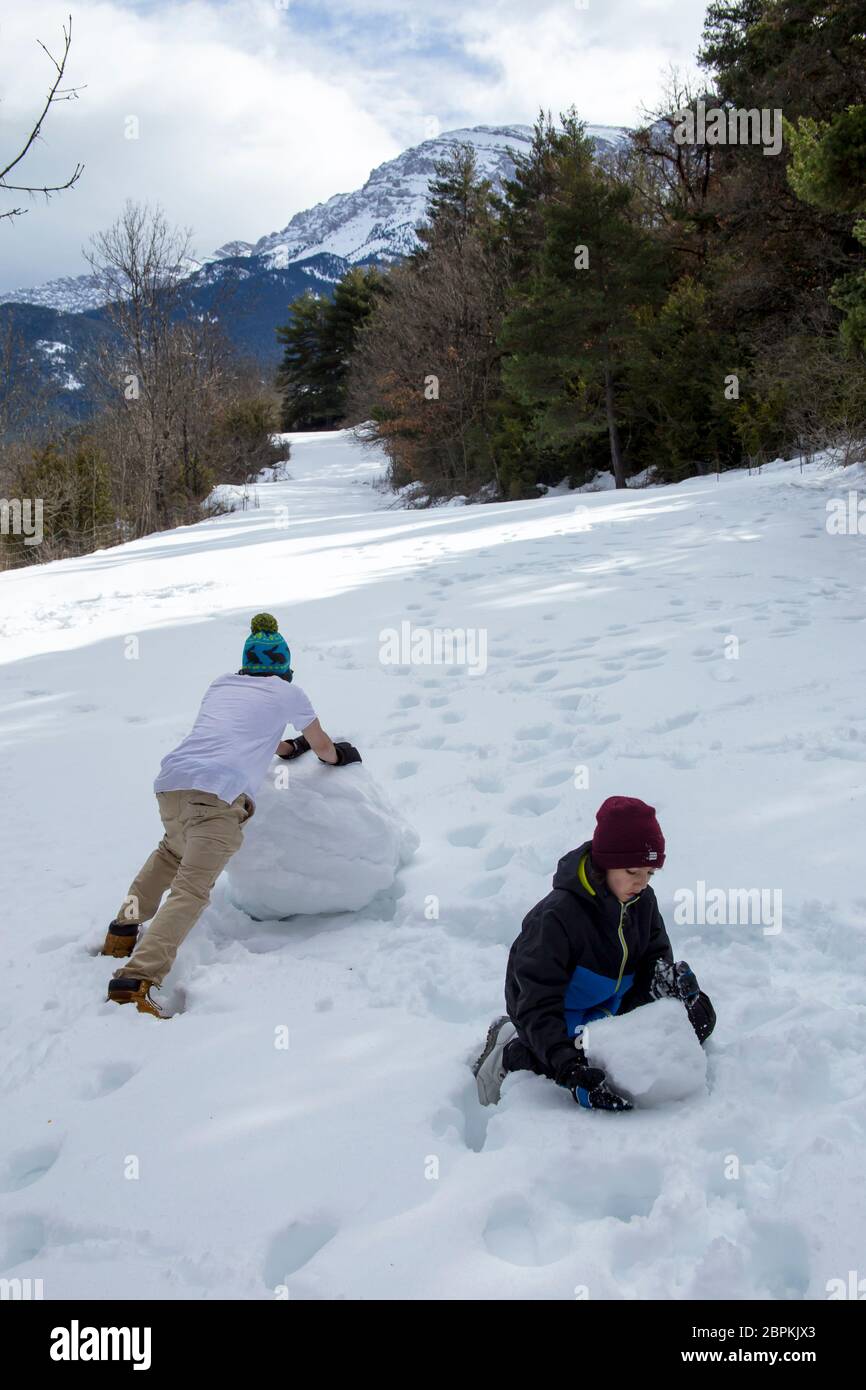 Ein junger Kerl in einem T-Shirt und eine Kappe macht einen Schneemann mit seinem jüngeren Bruder im Winter Wald an einem schönen sonnigen Tag. Stockfoto