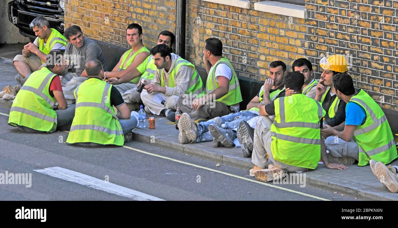 London Street Scene Gruppe von Bauarbeitern auf öffentlichen Bürgersteig vor der Baustelle sitzen hohen vis viz Jacken bei der Mittagspause Großbritannien Stockfoto